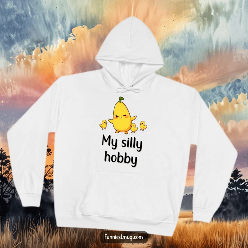 Funny hoodie featuring a plump banana character winking and juggling tiny rubber chickens, creating a humorous and cozy scene.